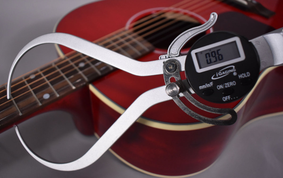 A digital caliper with a 0.96mm reading is measuring the string height above the fretboard of the cherry-finished acoustic guitar.