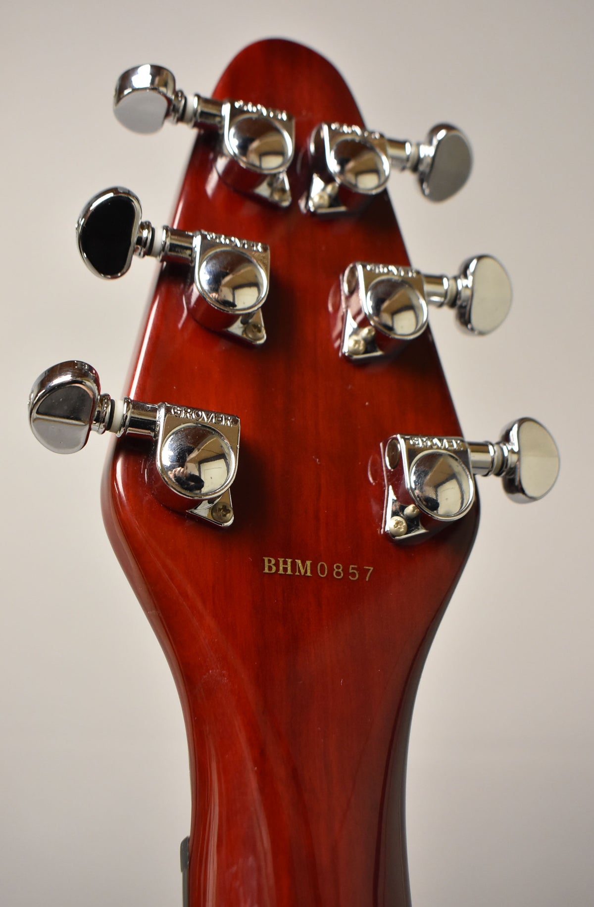 The guitar's cherry red headstock, viewed from the back, features six chrome tuning machines and a gold serial number BHM0857.