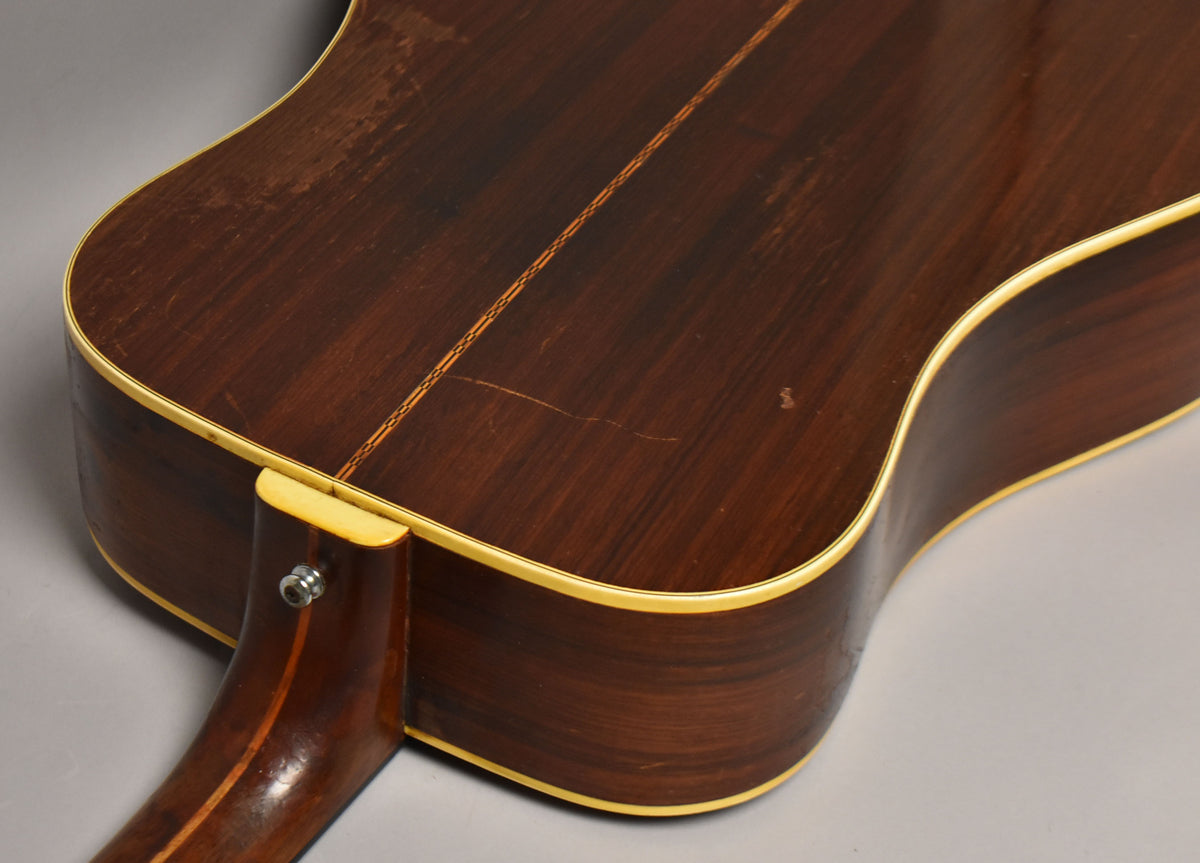 Close-up of the guitar's dark brown back and side, showing a light center strip, cream binding, and visible finish wear and scratches.