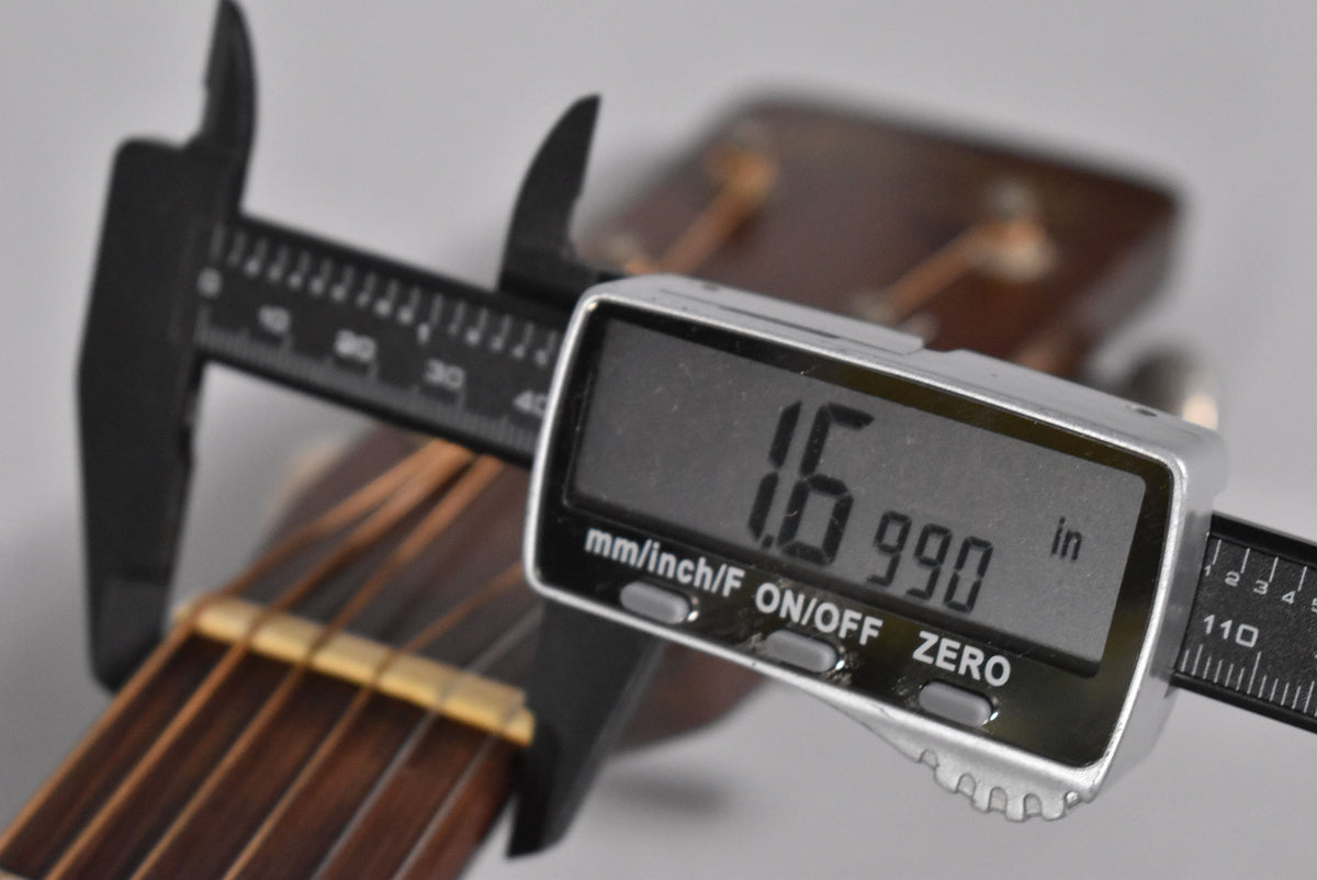 A digital caliper measures the guitar's nut width at 1.699 inches, with the dark brown fretboard and headstock visible.
