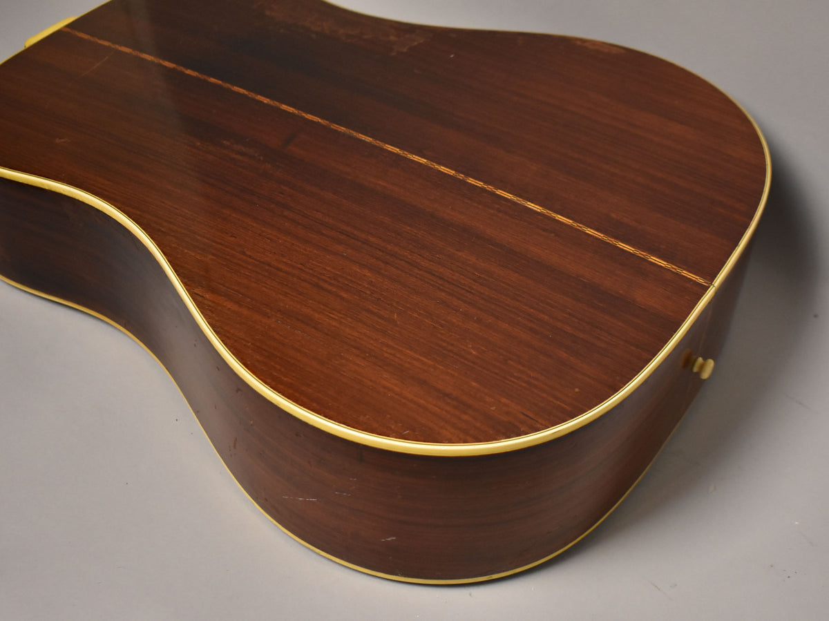 Close-up of the lower bout of a dark wood guitar back with a light center strip and binding, showing some wear.