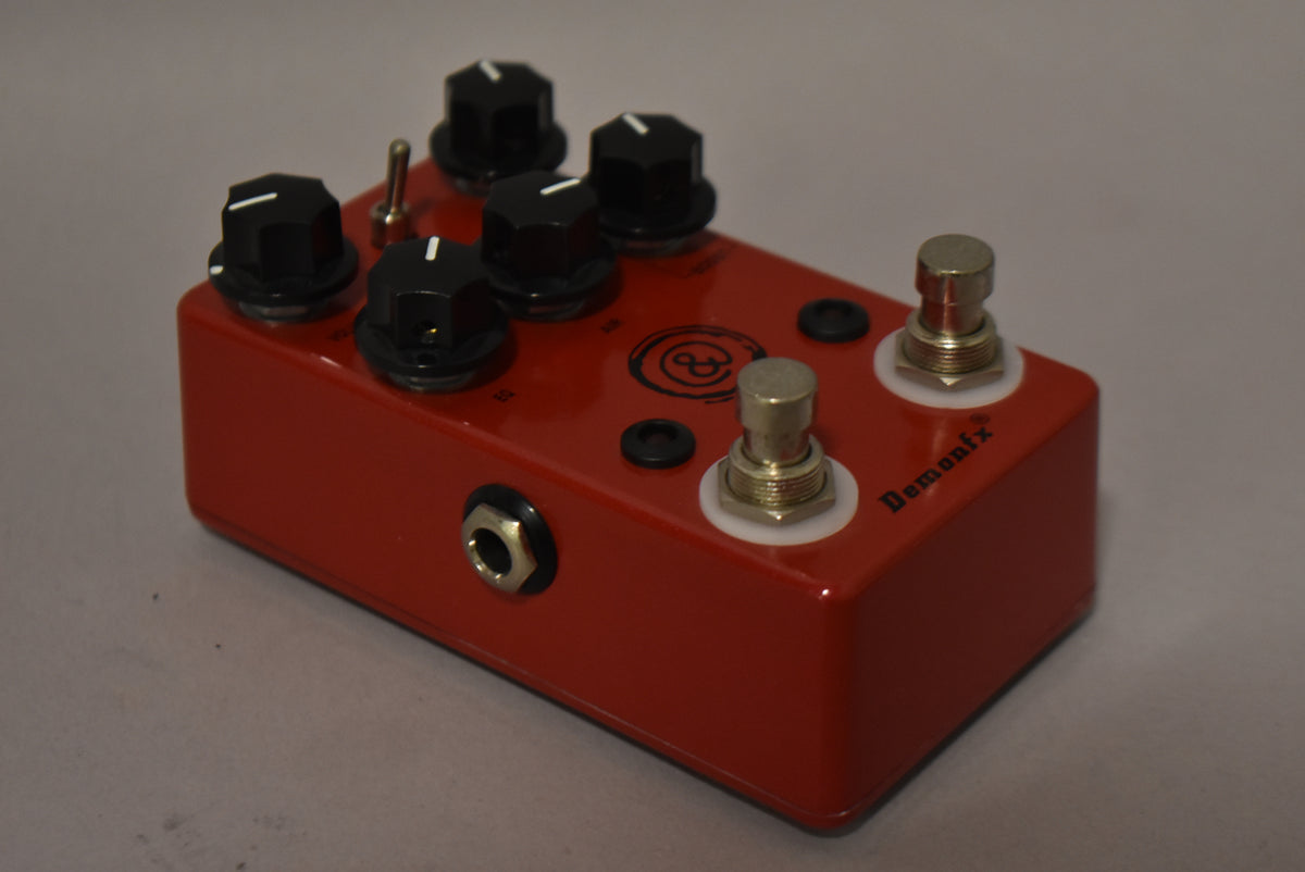 Red effects pedal, angled from the front-left, showing four black knobs, a toggle switch, two footswitches, and a side input jack.