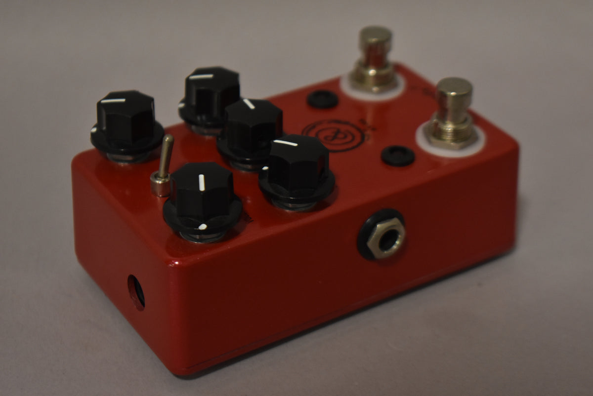A red metallic effects pedal, viewed from the front-right, with five black hexagonal knobs, a metal toggle switch, and two footswitches.