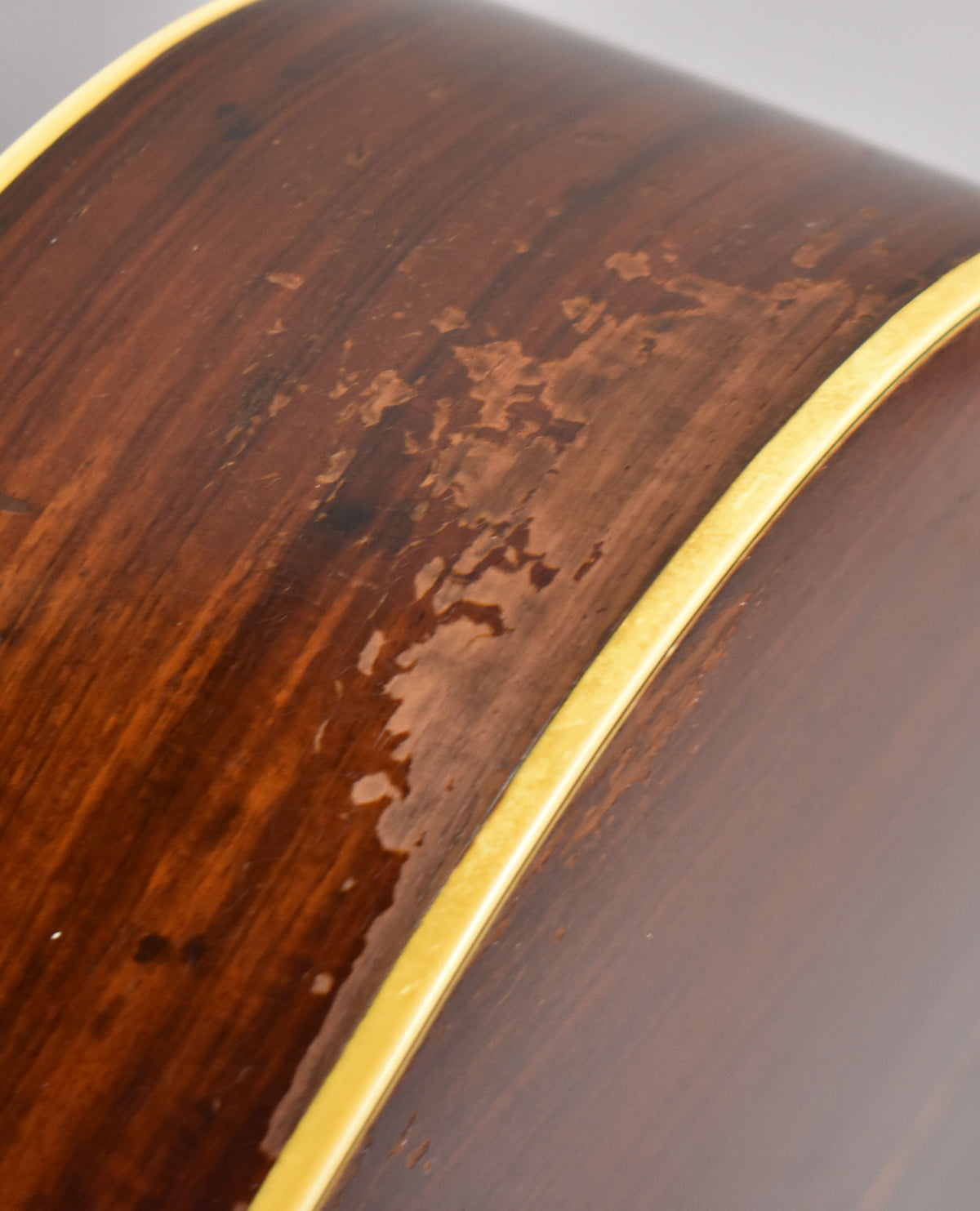 Close-up of the guitar's dark brown side, showing significant finish wear and flaking, with a cream binding strip along the edge.