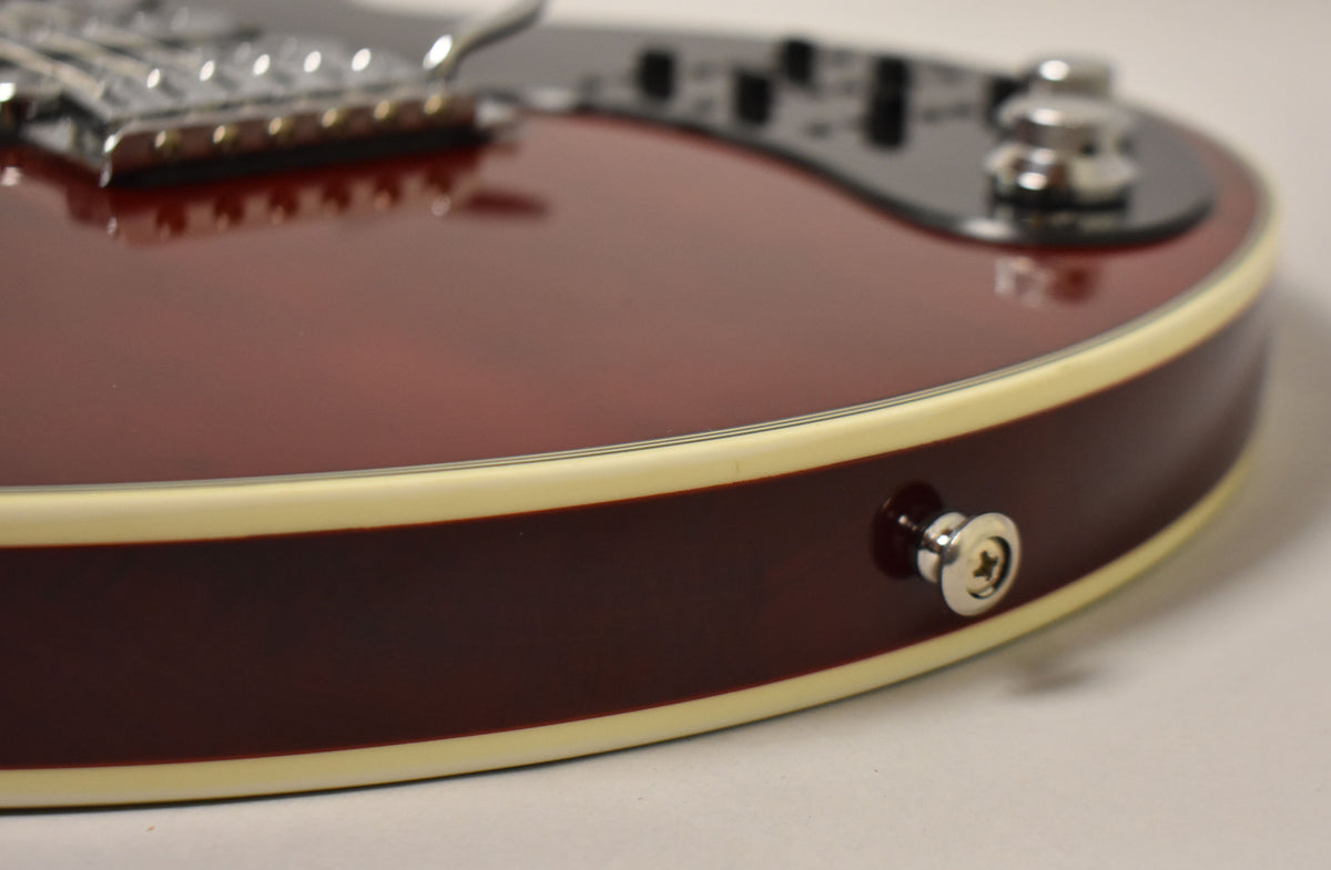 Close-up of the guitar's cherry red body, showing cream binding, a chrome strap button, and blurred bridge and controls in the background.