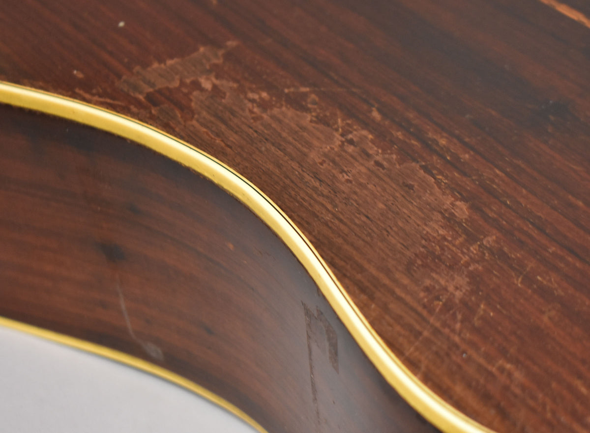 Close-up of the guitar's dark wood body with a light binding, showing significant finish wear and scratches on the upper bout.