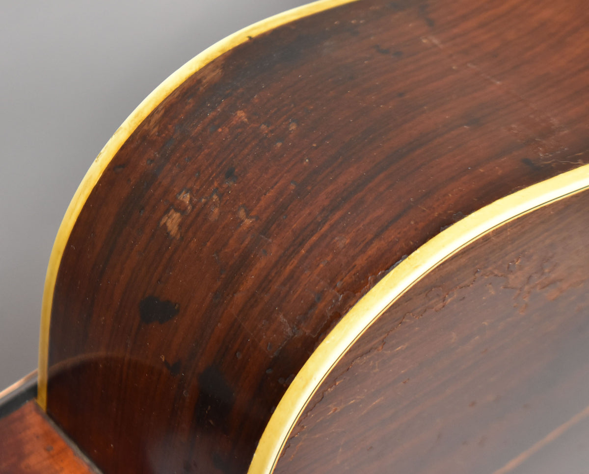 Close-up of the guitar's dark brown, worn side with visible wood grain and light binding, showing finish wear and checking.