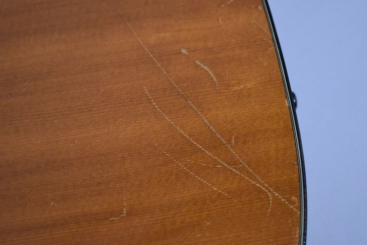 Close-up of the guitar's natural finish body, showing numerous scratches and wear marks across the wood grain.