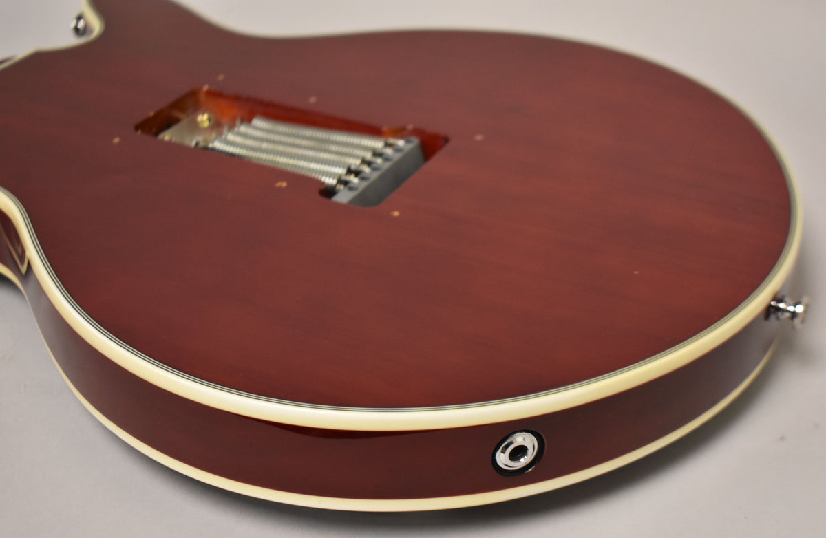 The cherry red guitar body, with cream binding, is shown from the back, revealing a tremolo spring cavity and output jack.