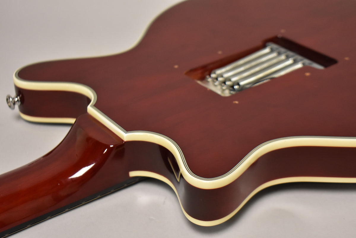 The cherry red guitar's back shows a tremolo spring cavity, cream binding, and the neck joint, with minor surface marks.