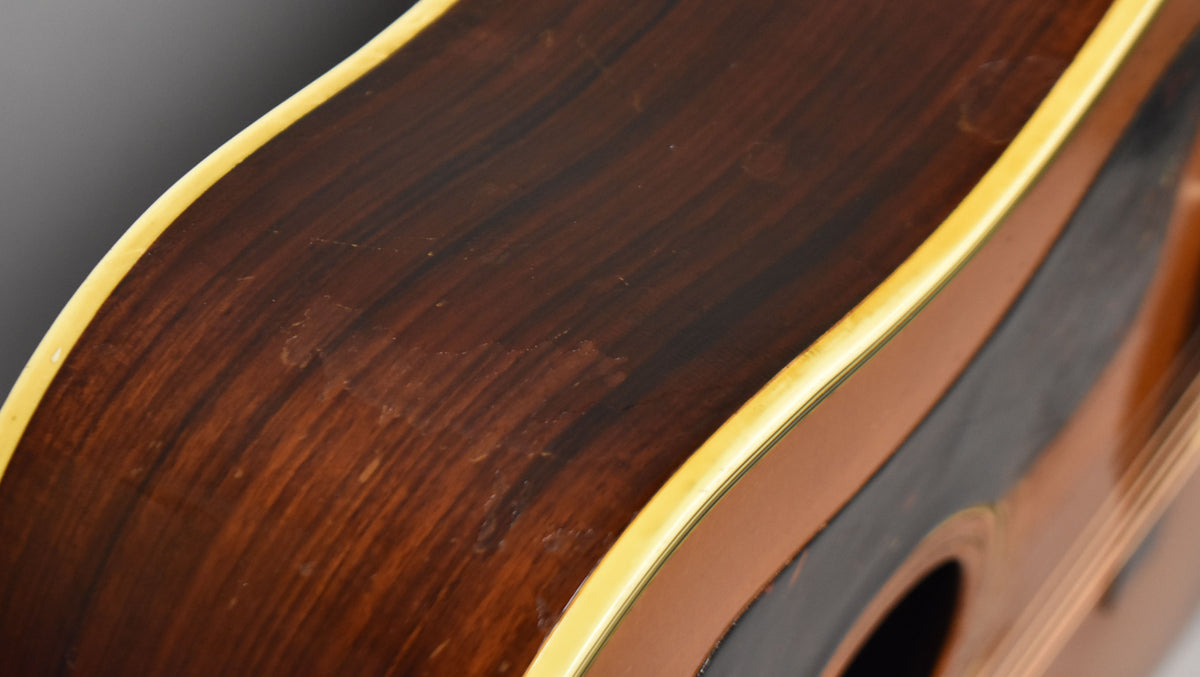 Close-up of the guitar's dark brown, worn side with light binding, showing scratches and finish wear near the soundhole.