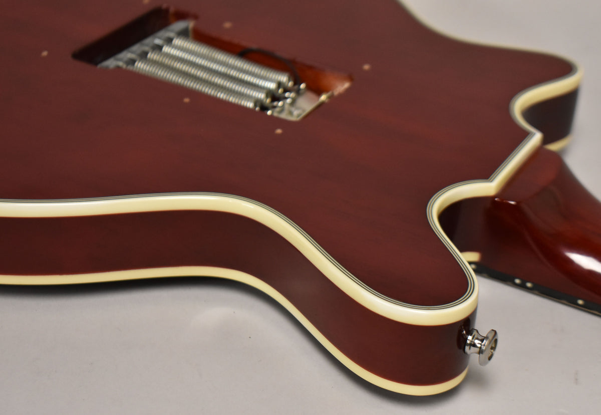 The guitar's cherry red body, with cream binding and black pinstripes, shows the tremolo spring cavity and a chrome strap button.