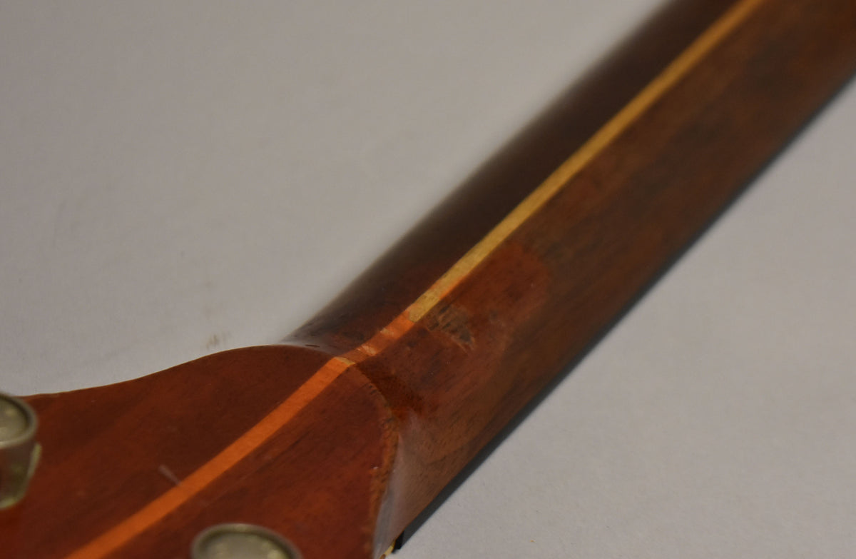 Close-up of the guitar's dark brown neck and headstock joint, showing a light wood stripe, a small ding, and two tuning pegs.