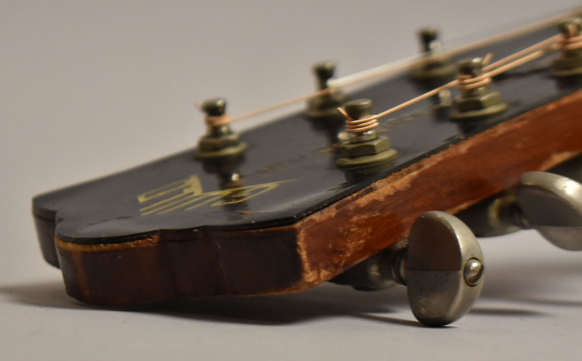 Close-up of the guitar's headstock, showing dark finish wear on the edges, with a gold logo and three metal tuners.