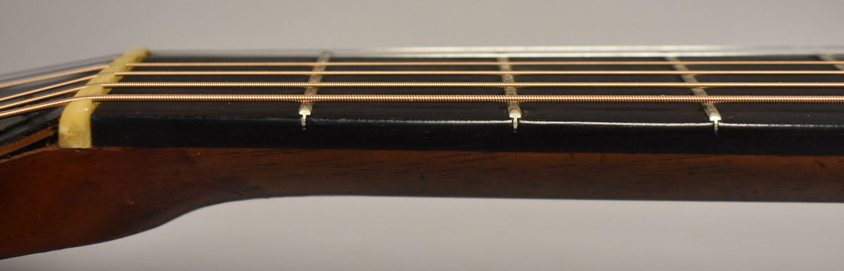 Close-up of the guitar's dark fretboard and nut from the side, showing light wear on the nut and frets, with bronze strings.