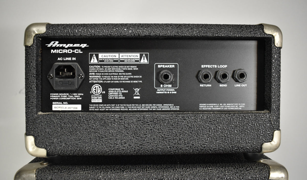 Rear view of the black textured amp head, showing the power input, speaker output, and effects loop jacks, with some wear on the metal corner protectors.