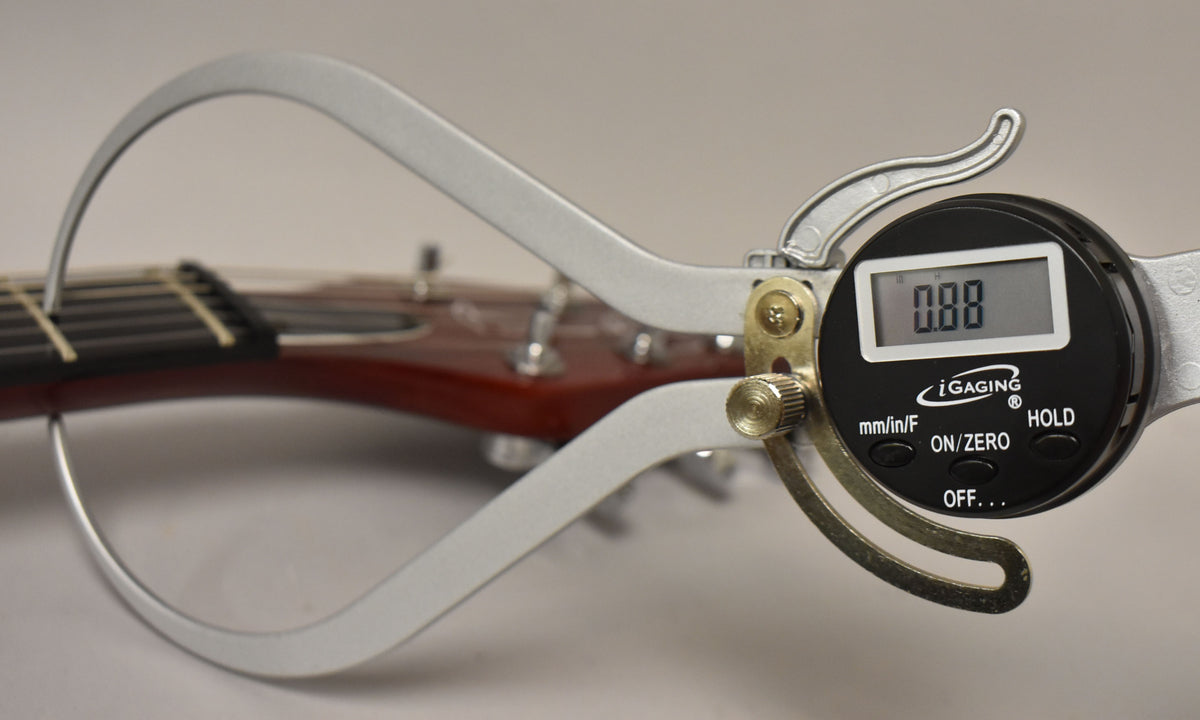 A digital caliper measures the string height above the frets on the cherry red guitar neck, displaying "0.88".