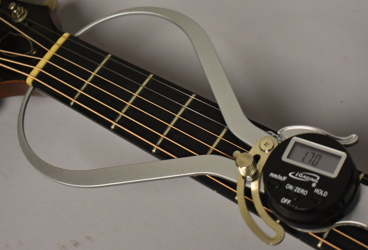 A digital caliper measures the nut width of the dark fretboard, showing "1.70" on its screen.