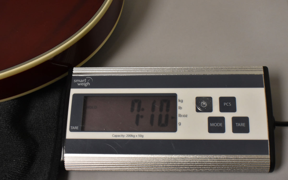 The cherry red guitar body, with cream binding, rests on a digital scale displaying "7.10" lbs.