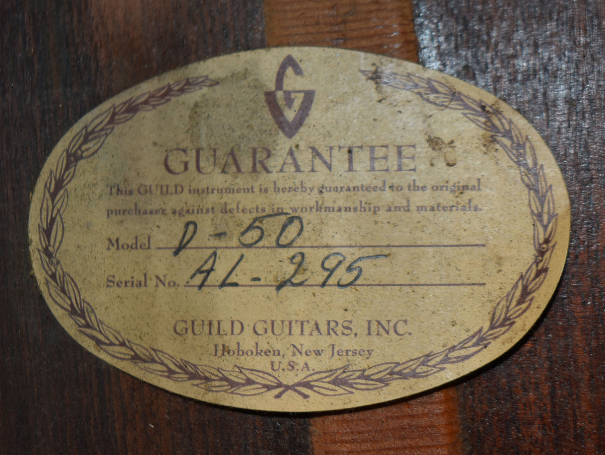 Close-up of the guitar's oval, aged paper guarantee label, showing handwritten model and serial numbers on a dark wood background.