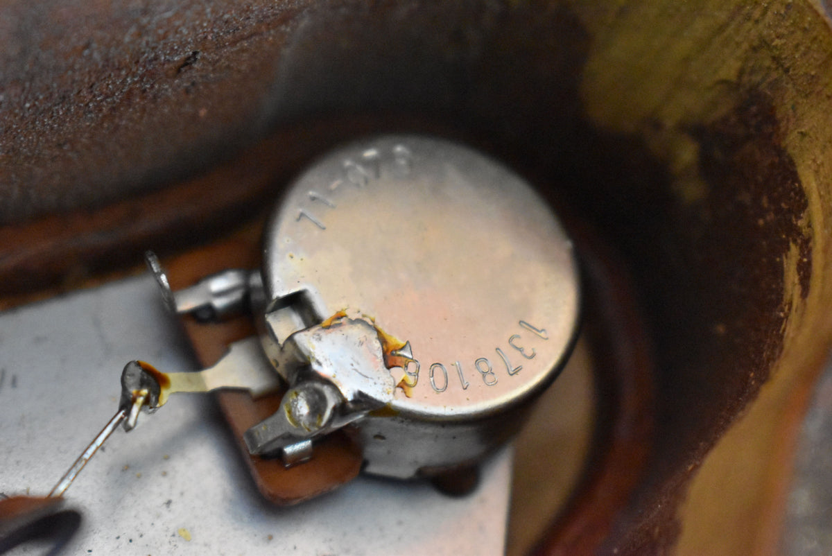 Close-up of a silver potentiometer with visible solder joints and stamped numbers, showing some corrosion and wear.