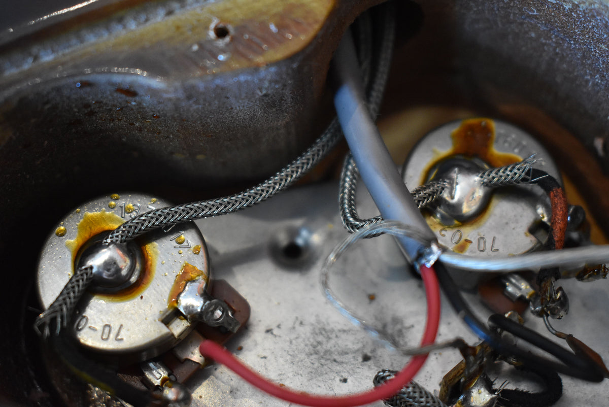 Close-up of the guitar's control cavity, revealing two silver potentiometers with soldered wires, some showing corrosion and wear.