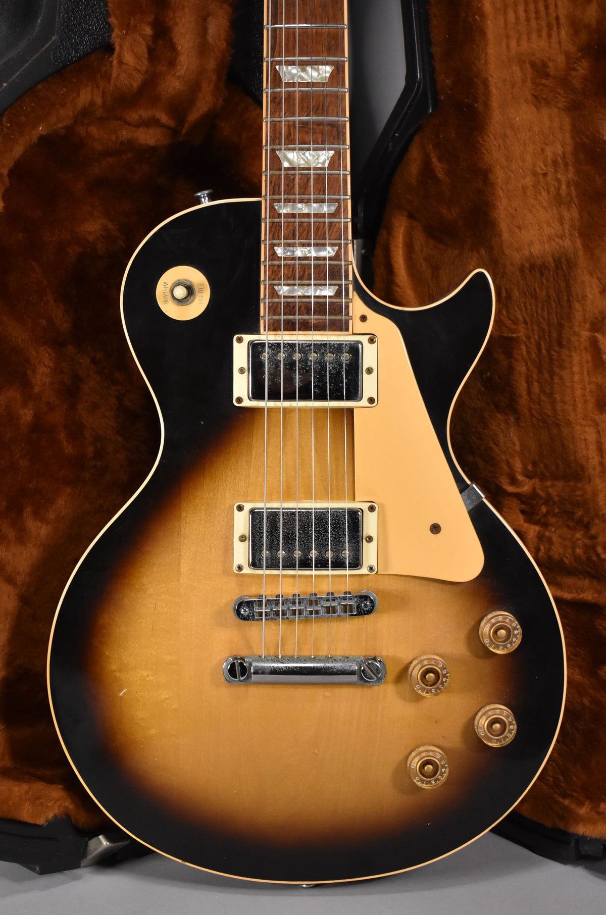 The guitar's tobacco sunburst body and neck are visible, with trapezoid inlays, cream pickguard, and four gold control knobs.