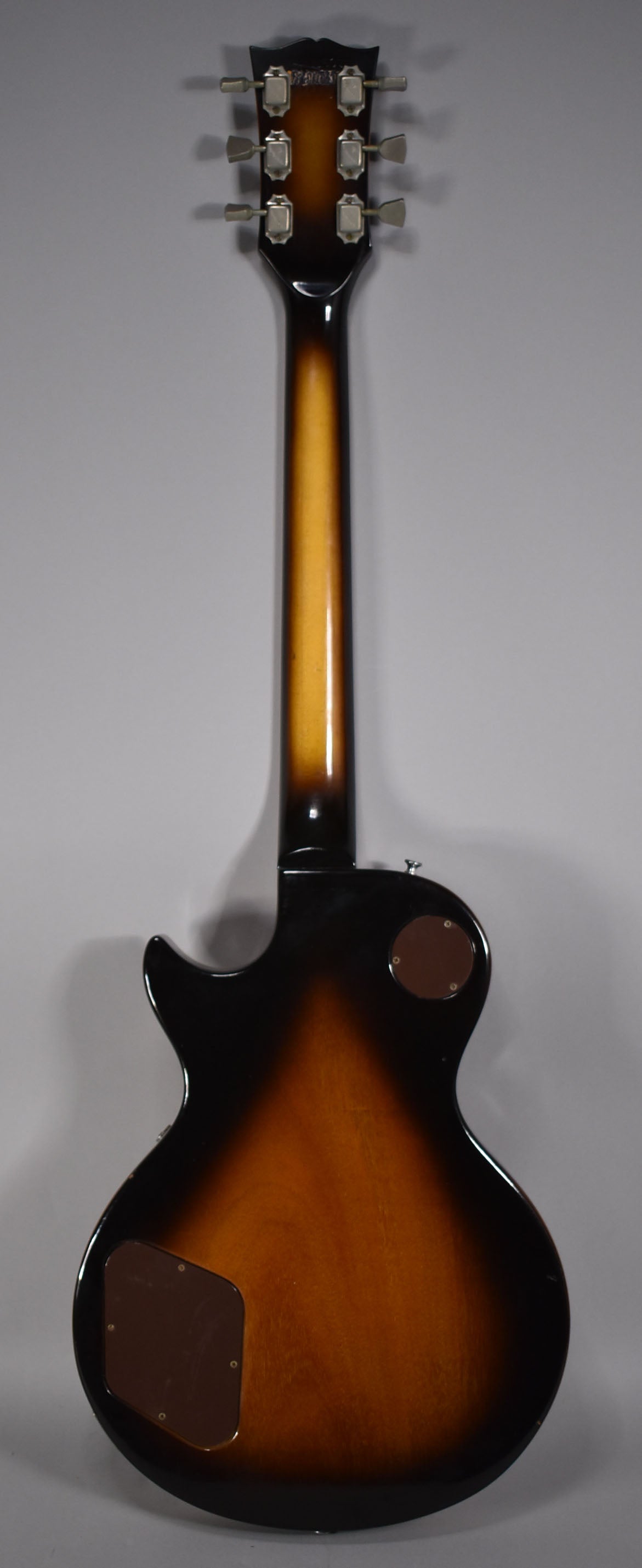 The back of a tobacco sunburst guitar, showing the headstock with six tuners, neck, and body with two brown control plates.