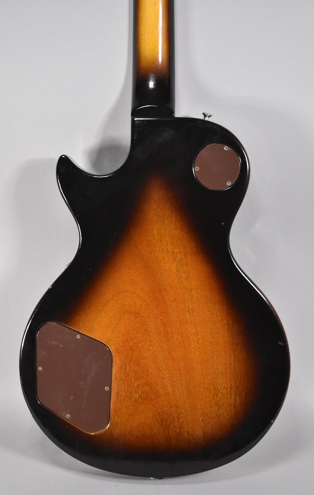 Full rear view of a tobacco sunburst Les Paul, showing the neck, body, and two brown control cavity covers.