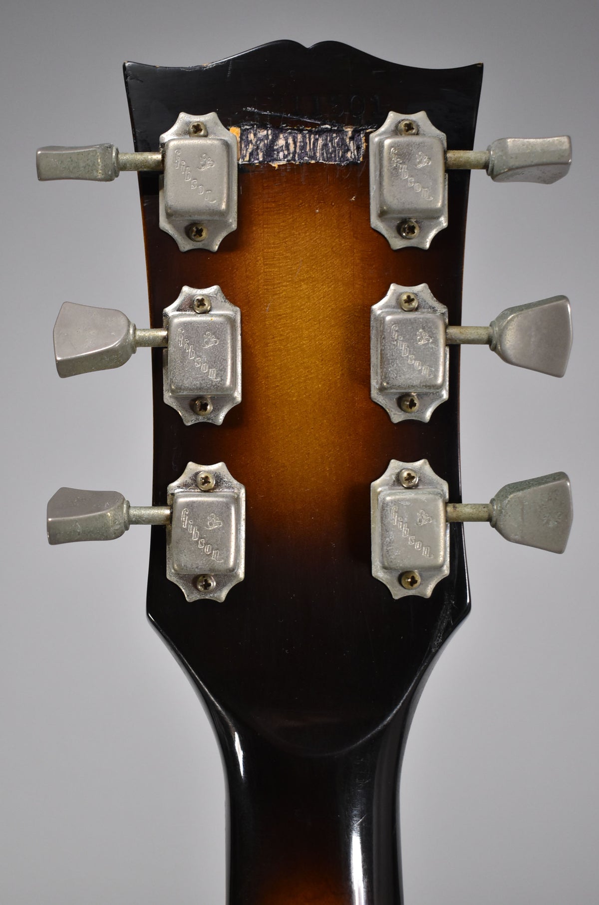 Rear view of the headstock and top of the neck, showing six worn, trapezoidal tuners and a chipped finish on the headstock.
