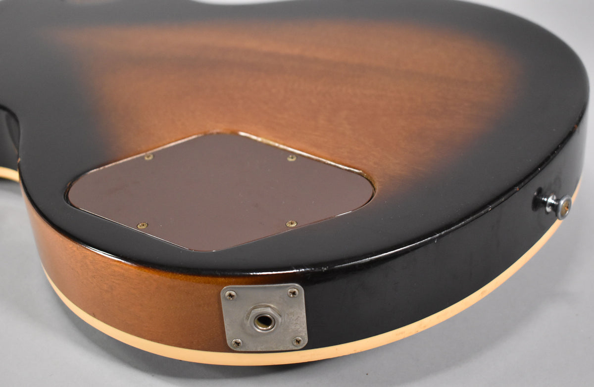 The lower bout of a tobacco sunburst guitar, showing the output jack, strap button, and control cavity cover.
