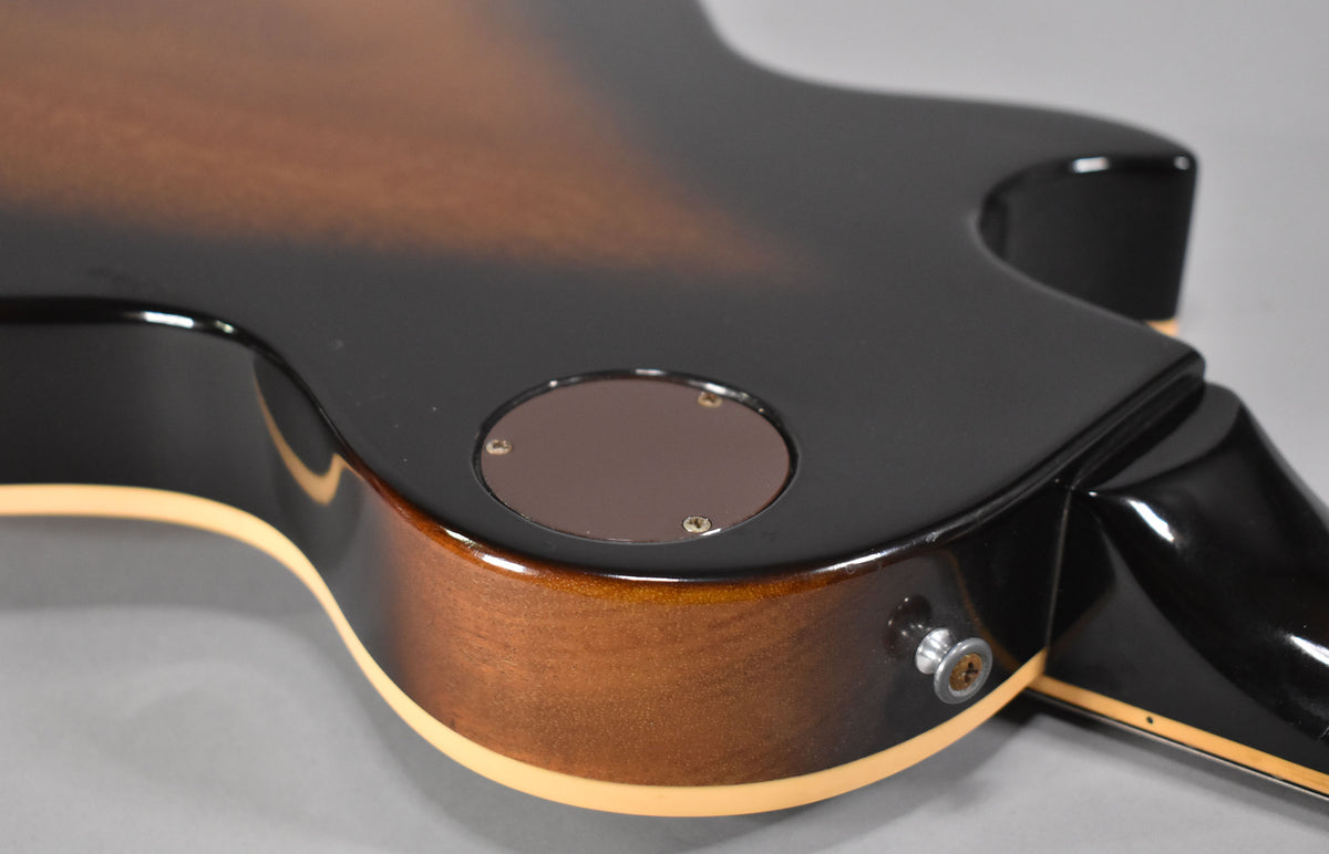Close-up of the guitar's lower back, showing the dark brown sunburst finish, cream binding, and the output jack with a strap button.