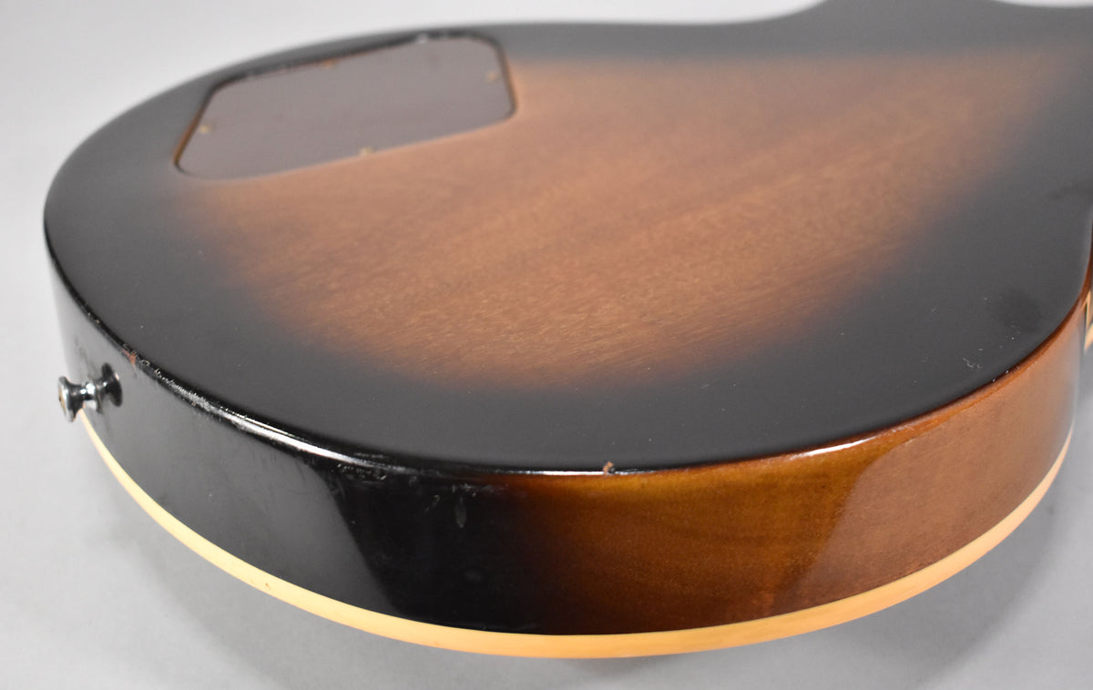 The guitar's lower bout, showing the tobacco sunburst finish, cream binding, and a visible chip on the dark edge.