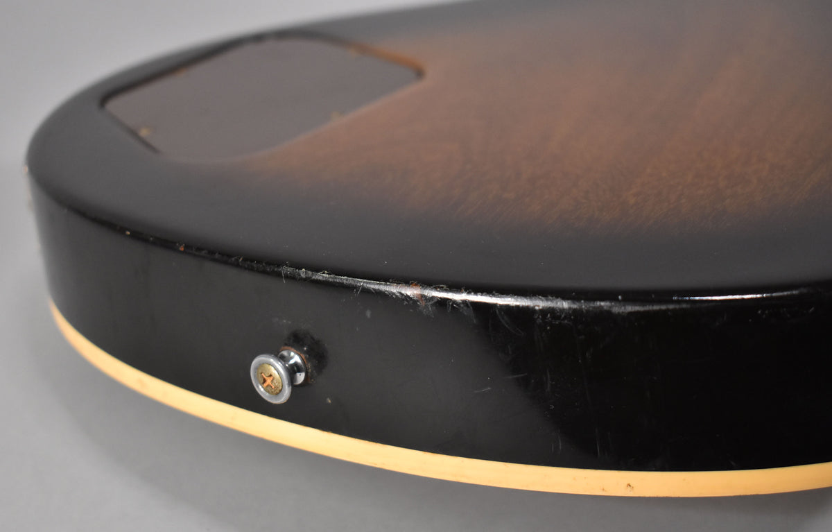 Close-up of the lower bout's tobacco sunburst finish, showing the input jack, strap button, and notable wear and scratches on the black edge.