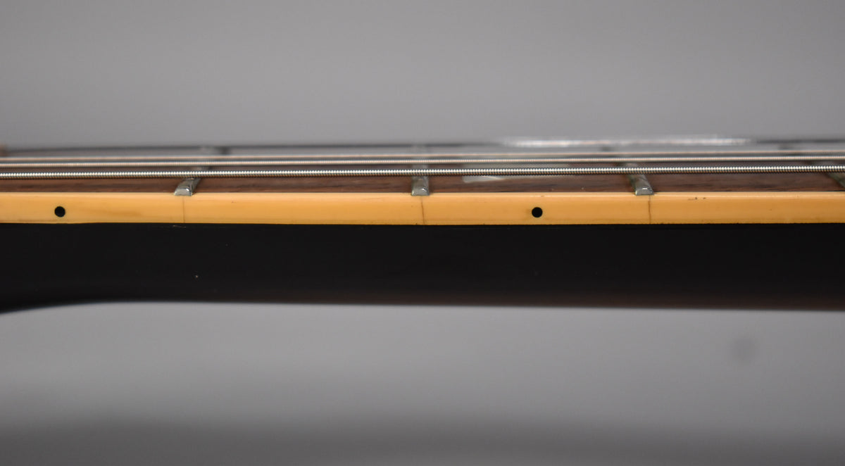 Close-up of the guitar's fretboard from the side, showing the dark wood, metal frets, and aged cream binding with side dots.