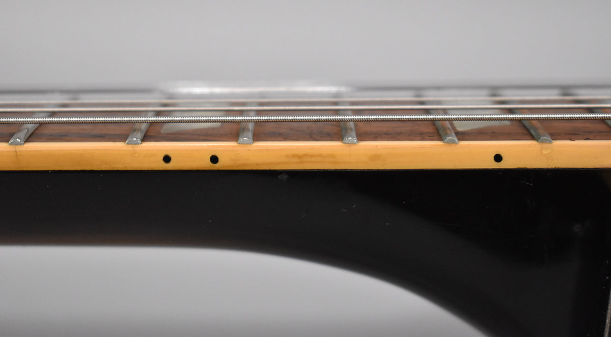 Close-up of the guitar's fretboard and neck binding, showing light wear and a few small black dots on the binding.