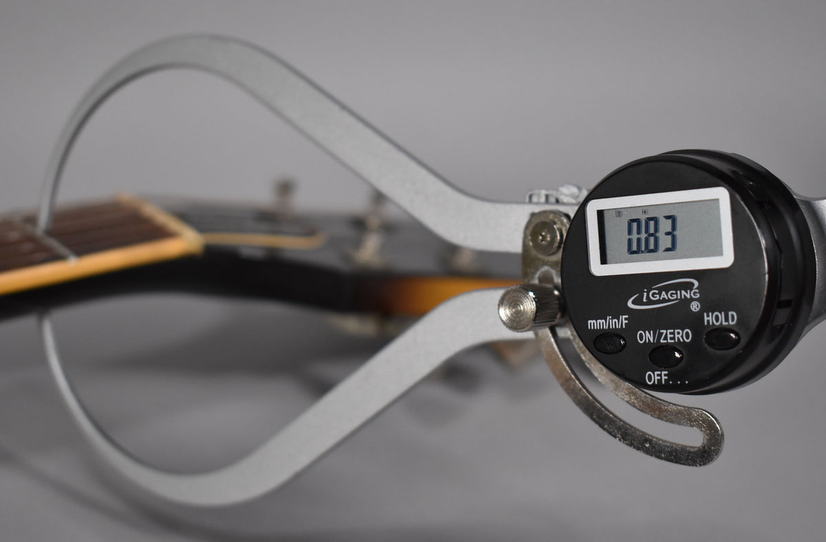 A digital caliper measures the guitar's fretboard, showing a reading of 0.83, with the tobacco sunburst finish visible.