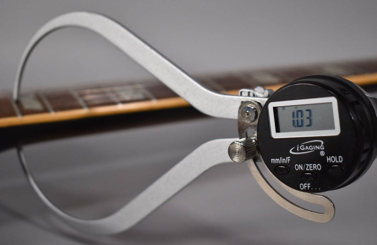 A digital caliper measures the guitar's fret height at 1.03mm, with the dark rosewood fretboard and frets visible in the background.