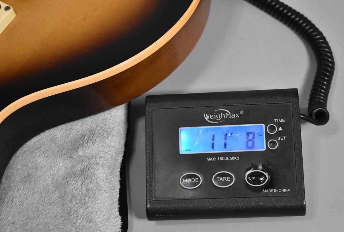 The guitar's lower bout in tobacco sunburst finish rests on a grey cloth, with a digital scale showing "11 LB 8 OZ".
