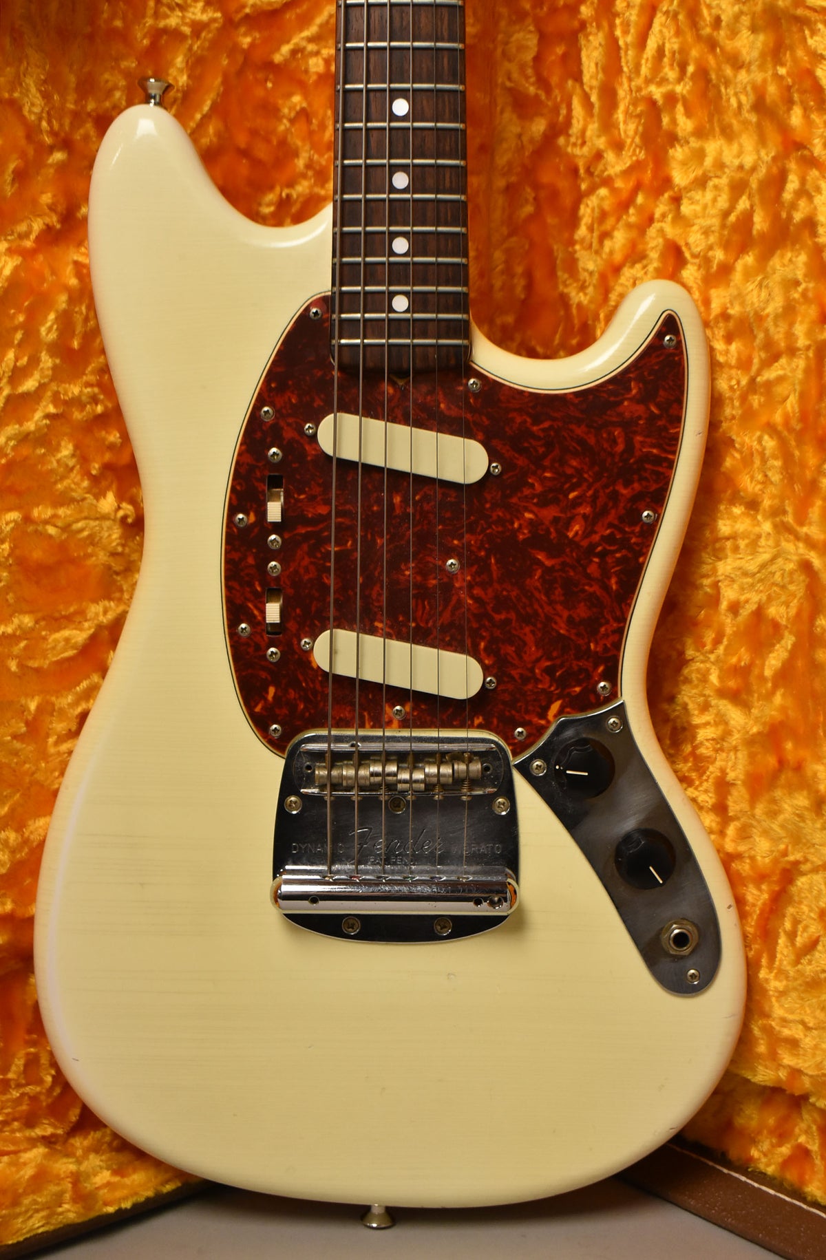 The Olympic White Mustang's body and neck are framed, showing a tortoiseshell pickguard, two cream pickups, and a vibrato bridge.