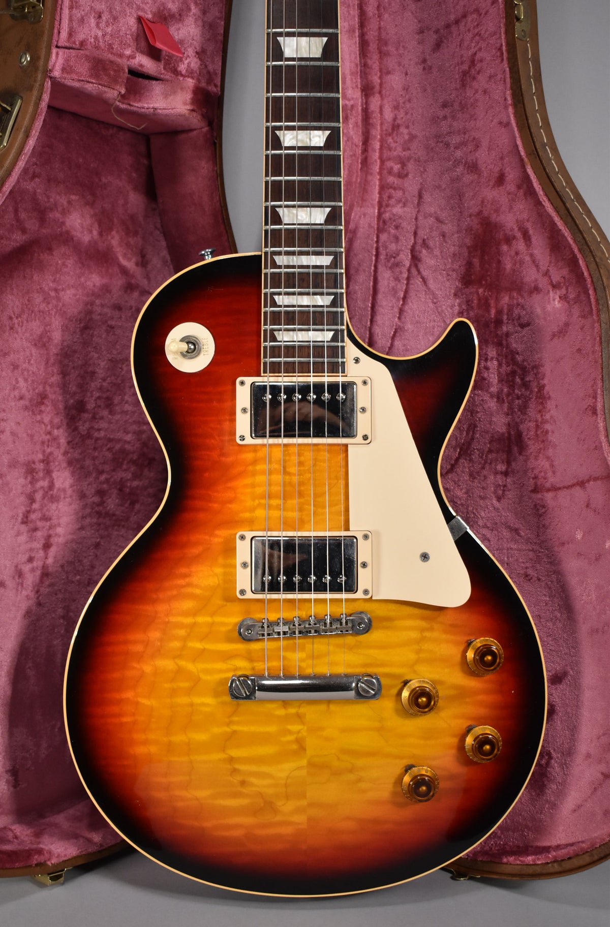 Full-frame view of a tri-burst flamed-top electric guitar with cream binding, pickguard, pickup rings, and trapezoid fretboard inlays.