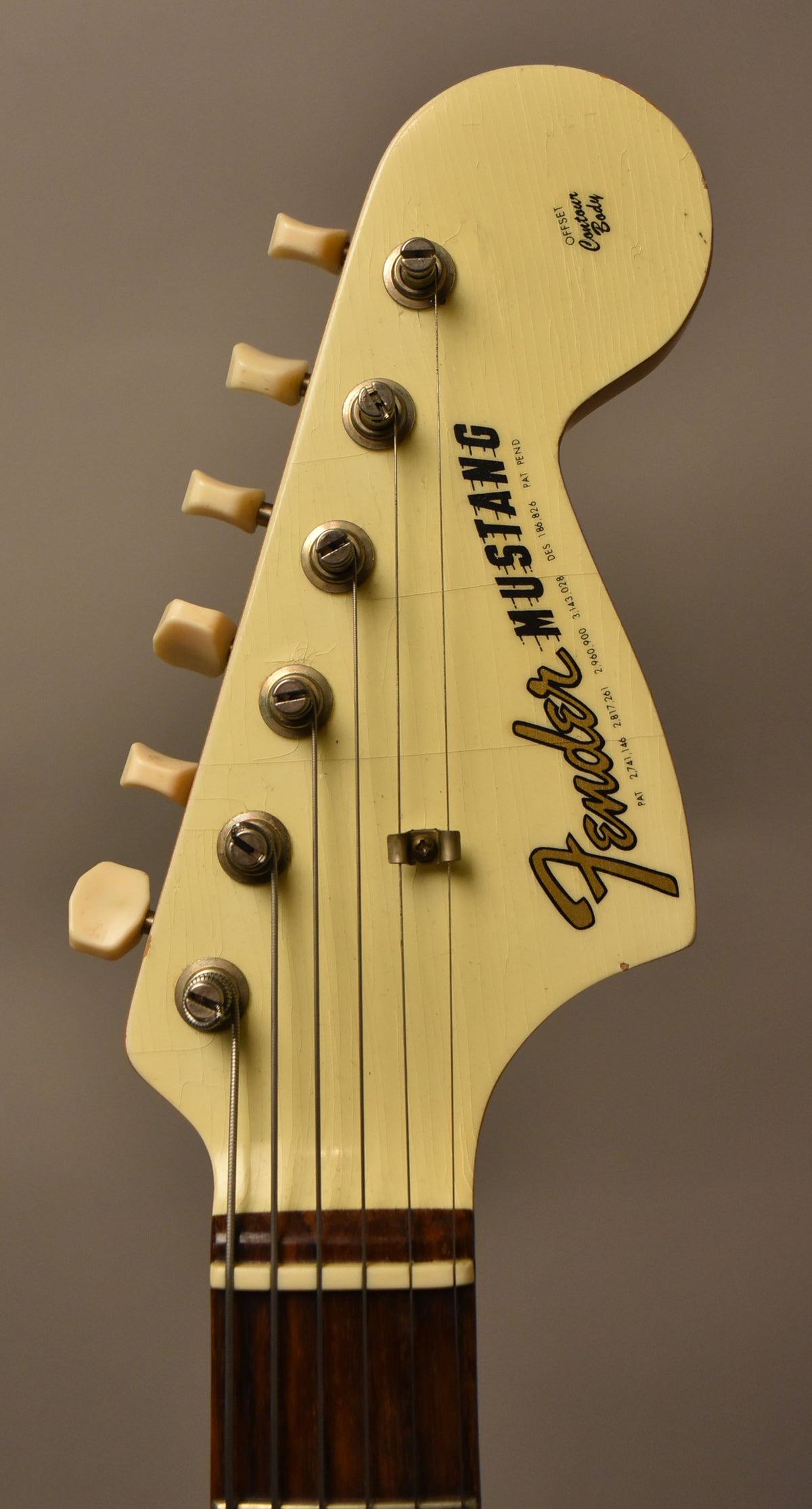 Close-up of the guitar's headstock, showing its aged Olympic White finish with extensive lacquer checking, six cream tuning pegs, and a string tree.