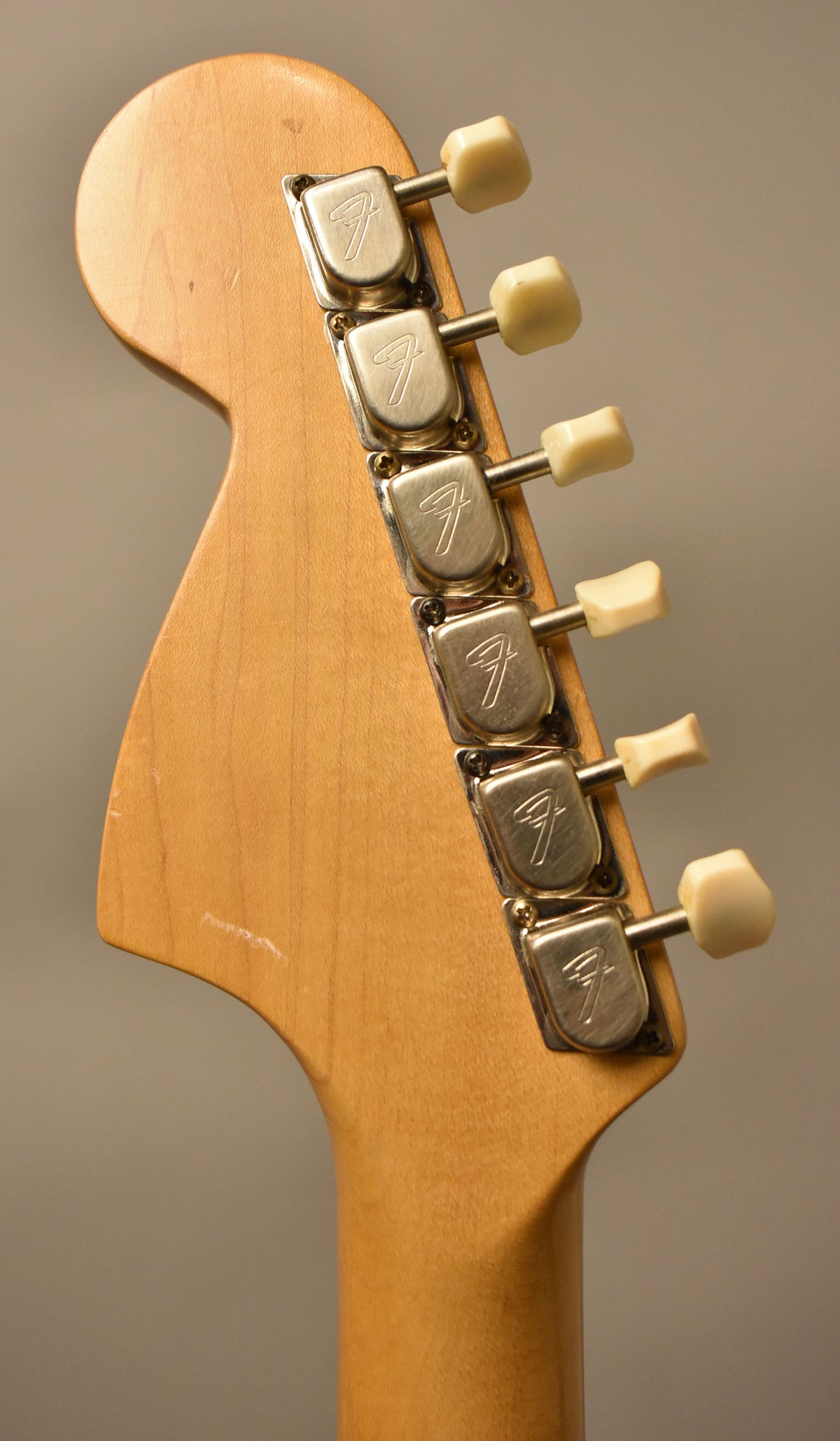 The back of the headstock and top of the neck, showing six cream-colored tuning pegs and light wear on the natural wood finish.