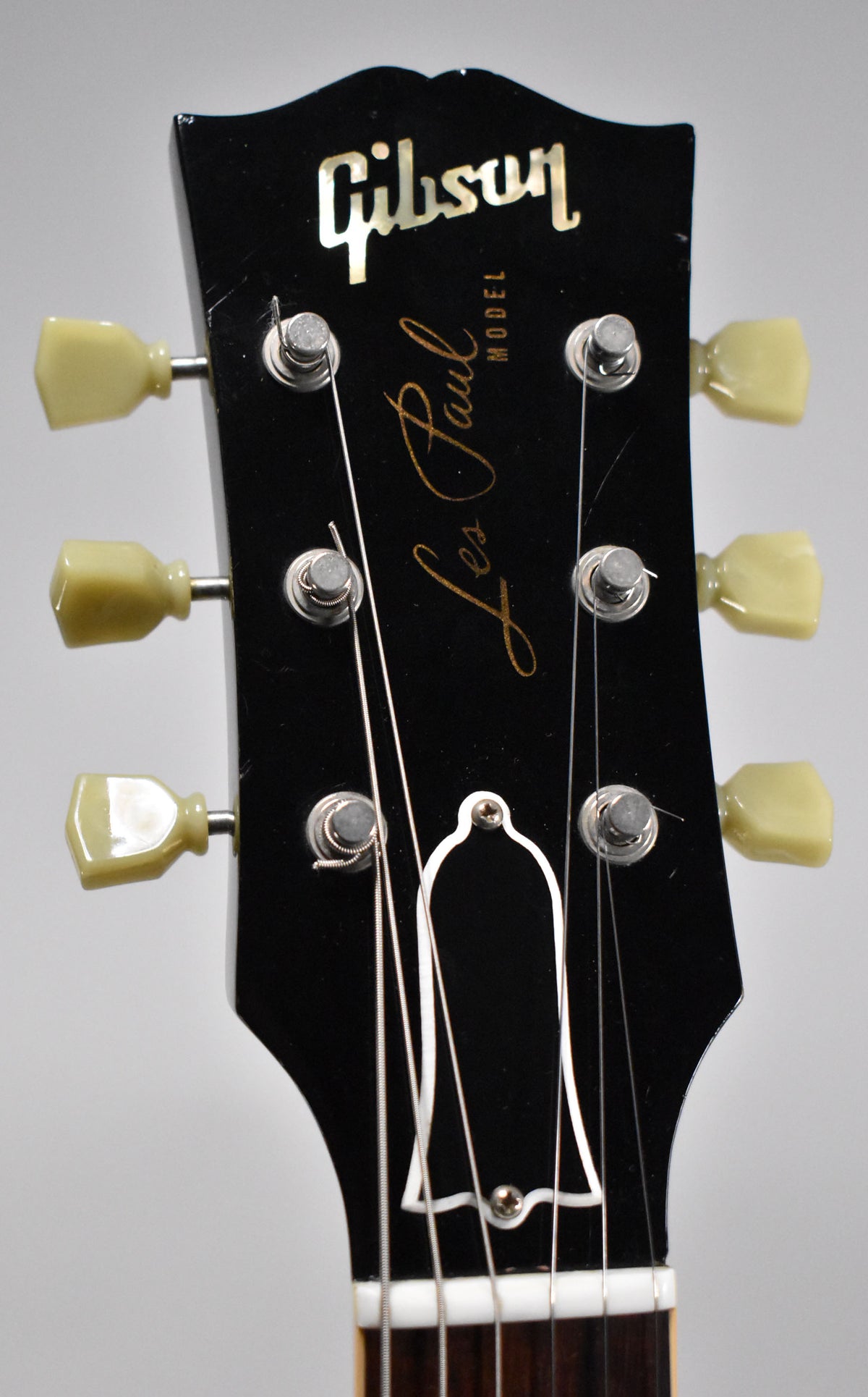 Close-up of the black headstock with cream tuning pegs, showing light scratches and a white bell-shaped truss rod cover.