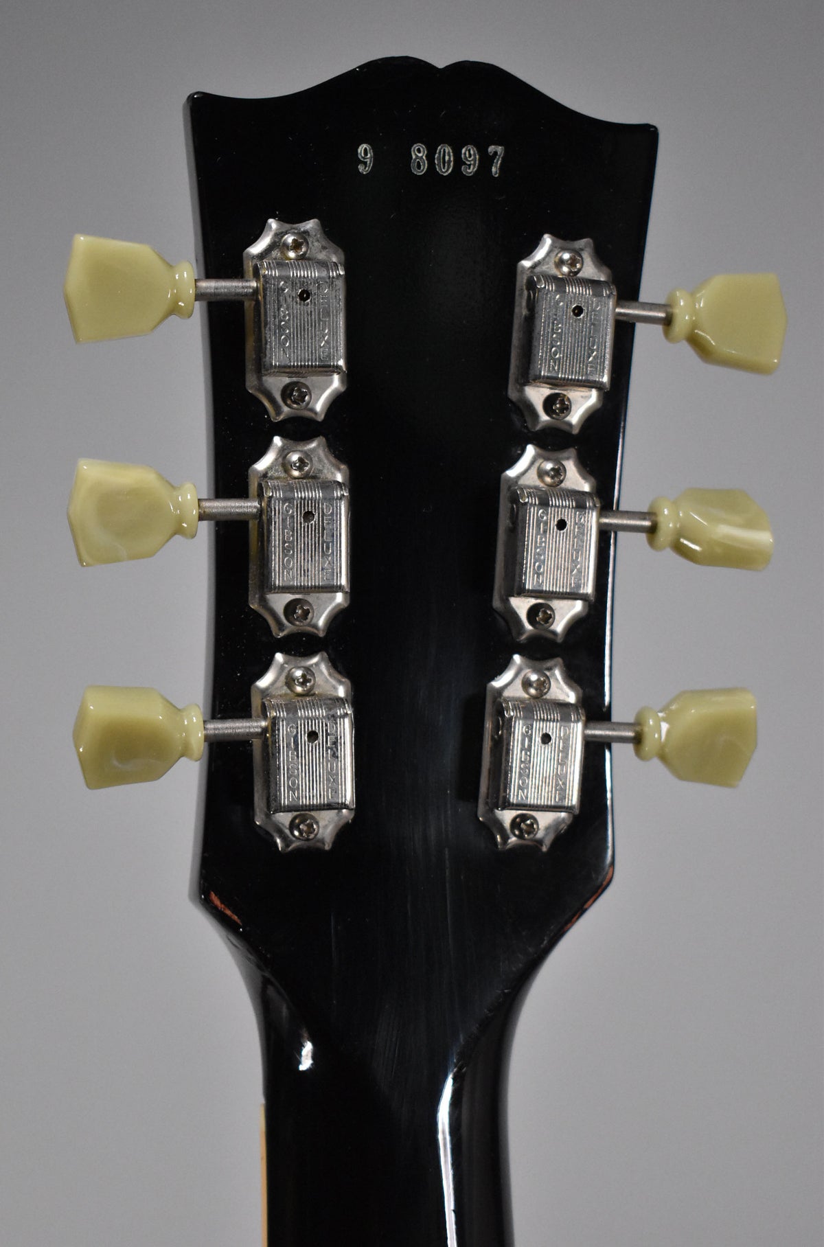 Rear view of the black headstock, showing six cream-buttoned tuners with chrome housings and a faint serial number.