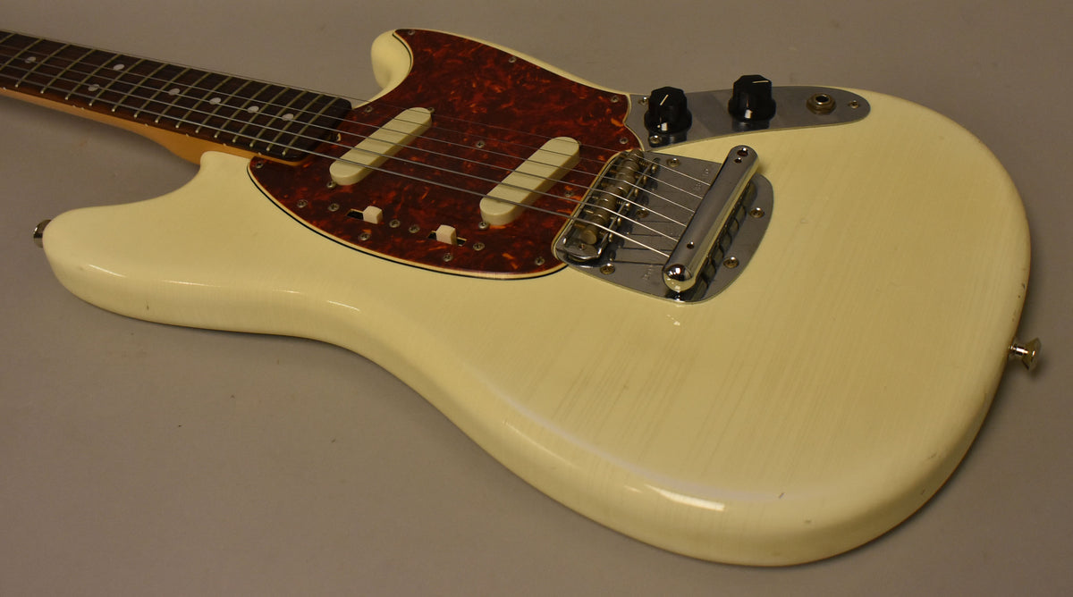 The Olympic White Mustang's body is angled from the neck, showing a tortoiseshell pickguard, two single-coil pickups, and chrome hardware.