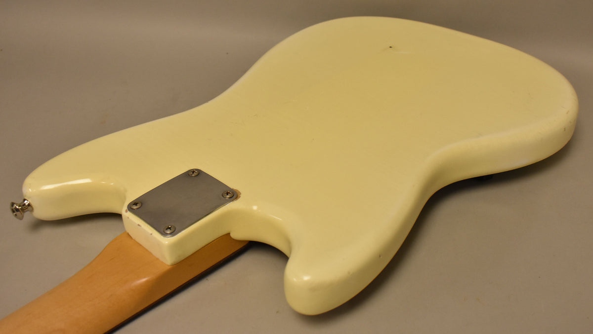 The back of an Olympic White electric guitar body, showing a metal neck plate, strap button, and light relic wear.