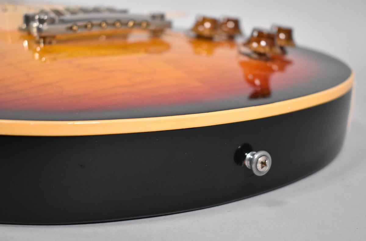 Close-up of the guitar's lower bout, showing the black back, cream binding, and the tri-burst top with four amber control knobs.