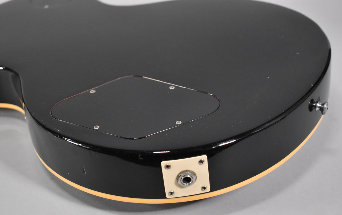 The guitar's black back and side are shown, with a cream output jack plate and control cavity cover, plus a strap button.