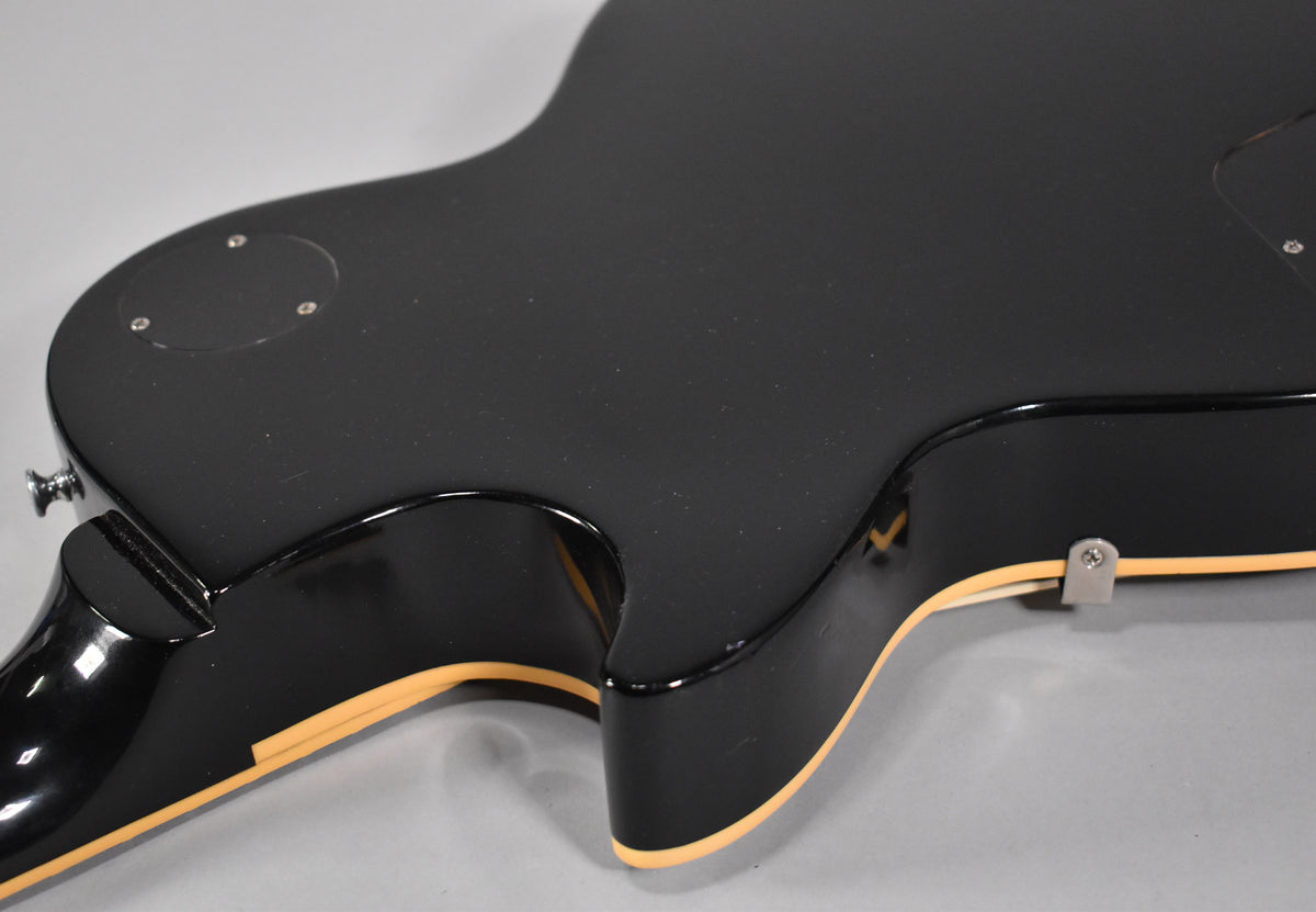The guitar's black back and sides are visible, with cream binding and a small metal strap button near the lower bout.